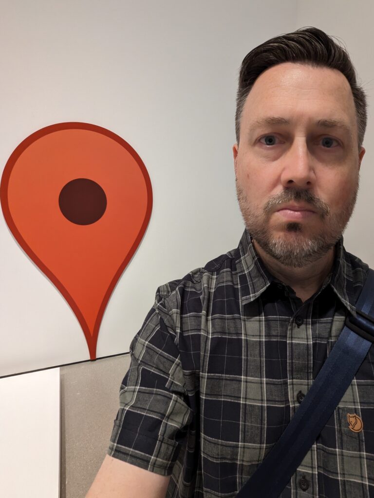 Stephen Francoeur standing in front of oversized reproduction of a red Google Map pin